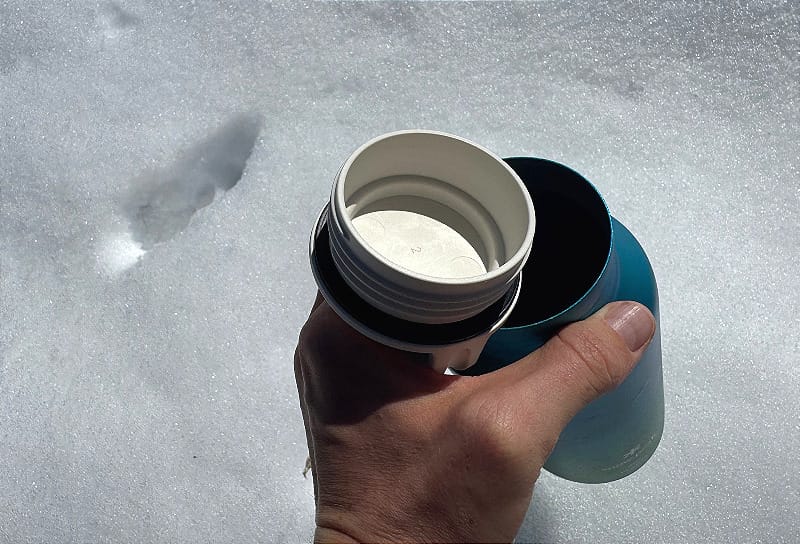 White cap detail of the Snow Peak Aurora Titanium Water Bottle laying on snow