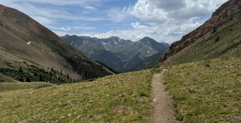 Colorado Trail winding through high alpine terrain in the San Juan Mountains with dramatic mountain views and cloudy sky.