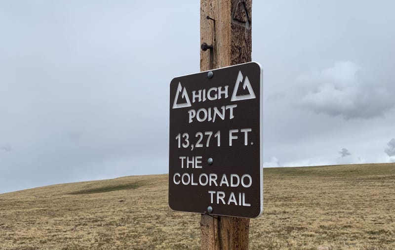 Wooden sign marking Coney Summit, the high point of the Colorado Trail at 13,271 feet, with cloudy sky in background.
