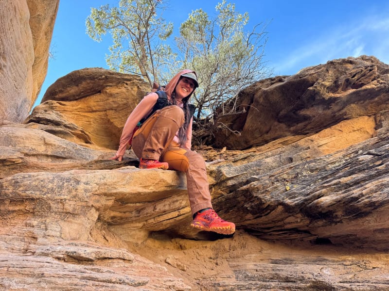  Woman wearing Fjällräven Keb Trousers Curved while hiking in slickrock terrain, sitting on a sandstone ledge with a backpack and trail shoes.