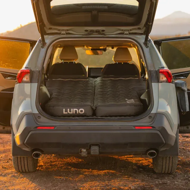 Fully inflated Luno Air Mattress 2.0 set up in the back of an SUV, with the hatch open at sunset in the desert.