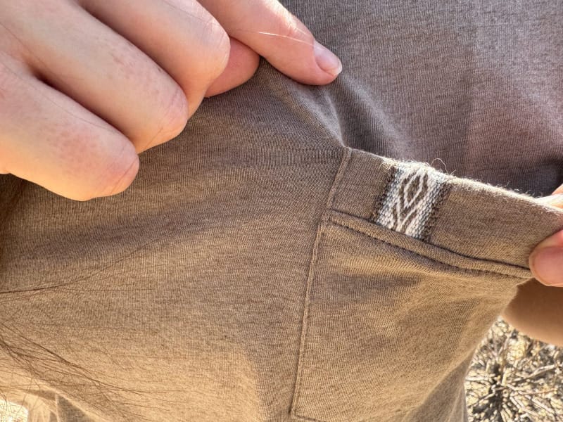  Close-up photo of the pocket detail on the Paka Pocket Tee, highlighting the woven accent tag and soft alpaca-blend fabric texture.