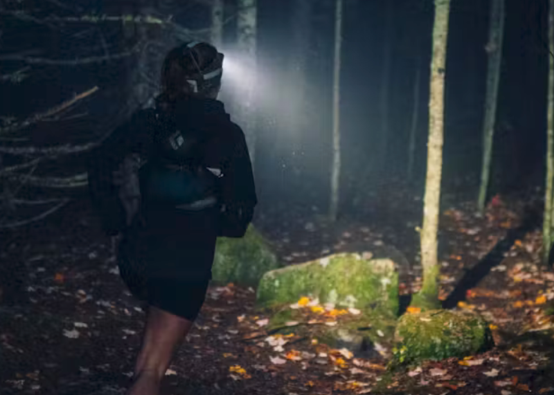 Trail runner wearing the Black Diamond Distance 1500 headlamp at night in a forest, beam lighting up the trail ahead.