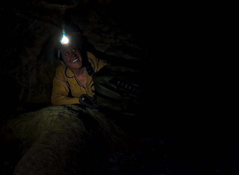  Person crawling through a narrow cave wearing the Black Diamond Distance 1500 headlamp, illuminating dark rock surroundings.