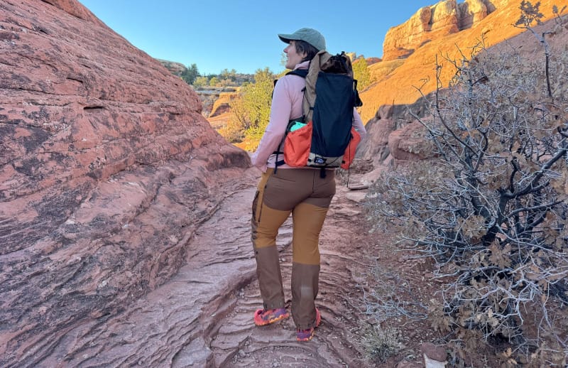  Woman standing in a desert canyon wearing Fjällräven Keb Trousers Curved, smiling with arms outstretched against sandstone walls.