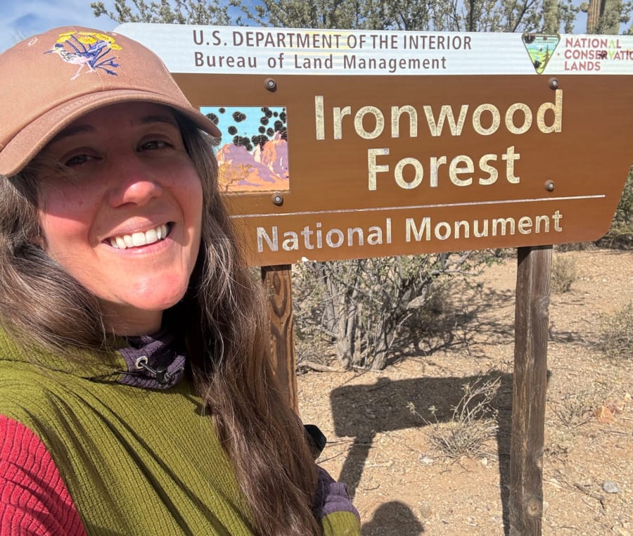  Woman wearing a color-blocked SAMBOB Microgrid Hoodie smiling in front of the Ironwood Forest National Monument sign in the Sonoran Desert.