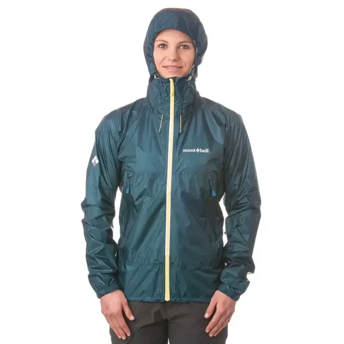 Woman modeling the Montbell Versalite rain jacket in dark green with hood up, zipped to the top.