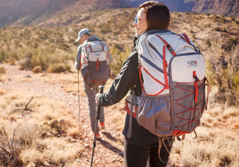 Hikers wearing Near Zero backpacks on a sunny desert trail surrounded by red rock formations.