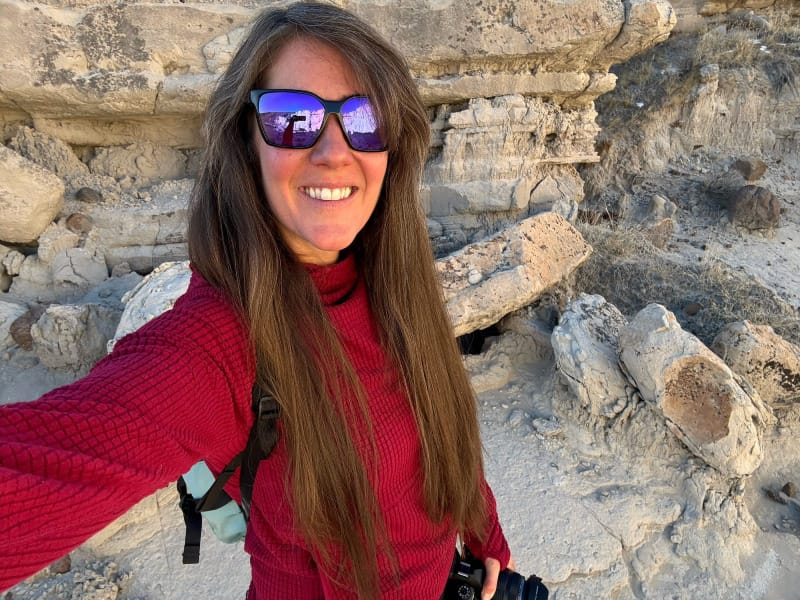 Hiker wearing a red waffle-knit hoodie smiles in front of desert rock formations during golden hour.