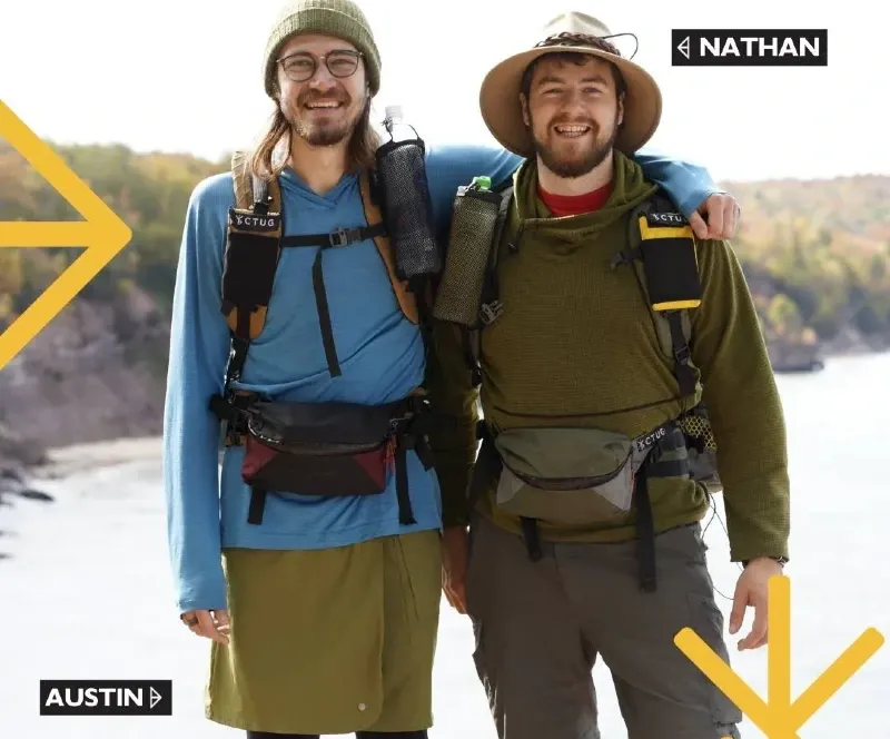 Austin and Nathan, co-founders of Chicken Tramper Ultralight Gear, smiling in hiking gear near a scenic river.