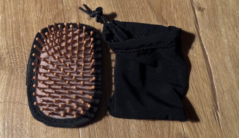Close-up of the Chicken Tramper Ultralight Gear Hiker Hairbrush with wooden bristles and included black carry pouch on a wooden surface.
