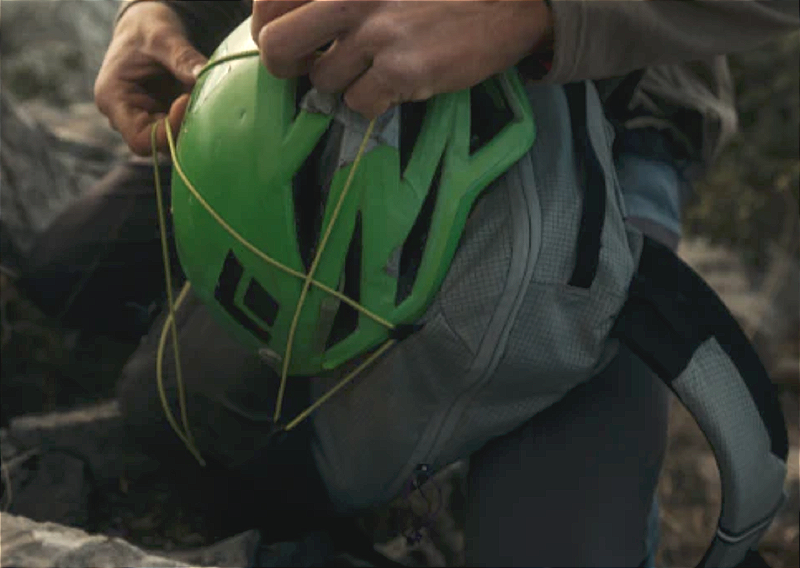 Close-up of a green climbing helmet strapped to a Gossamer Gear Cima 15 backpack using front bungee cord.