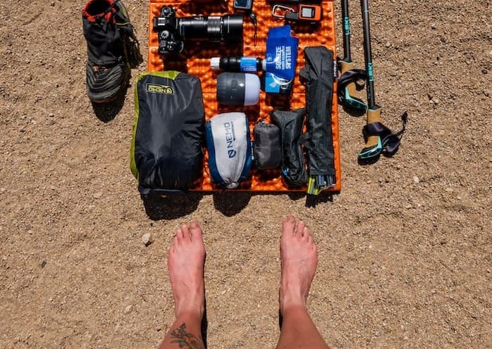 Flat lay of ultralight hiking and photography gear arranged on an orange foam pad, including camera equipment and trekking poles.