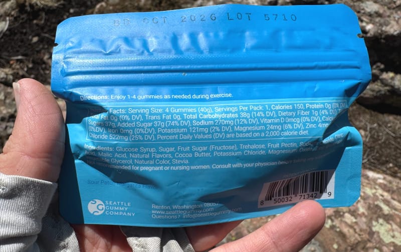  Nutrition facts and ingredients list on the back of a HydraFuel Hydration Gummies package held outdoors on a rocky surface.