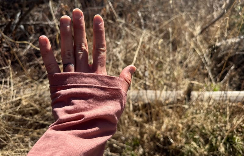 A hiker shows off the thumb loops on the sleeves of the Ibex Springbok Sun Hoodie in a forest setting.