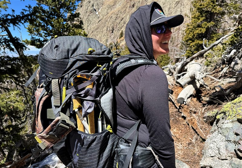 NEMO Persist 45L Backpack on a hiker with trekking poles on a rocky mountain trail.