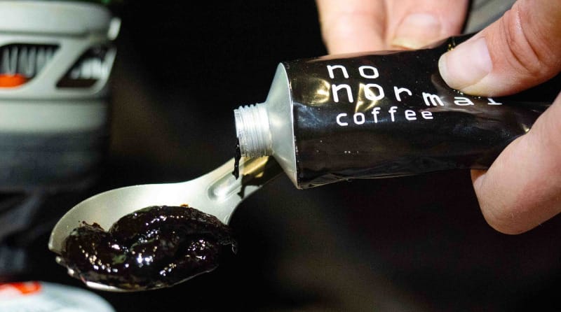 Close-up of No Normal Coffee being squeezed from a tube into a spoon, showing its thick, dark coffee paste consistency.