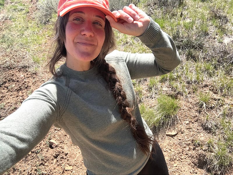  Woman wearing the green PAKA Ultralight COOLPLUS Crew while hiking in a grassy, sunlit trail area