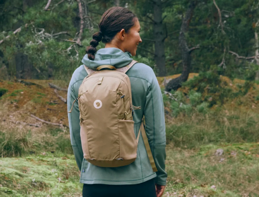 A woman wearing the Fjallraven Abisko Softpack 16 in a forested area, showcasing the compact and lightweight design for Summer 2025.