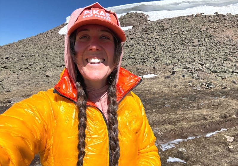  Woman wearing orange and yellow Enlightened Equipment Torrid Jacket smiling after a hike in the mountains.