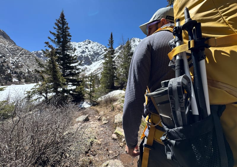 Backpacker wearing a yellow pack with LEKI Skytera FX Carbon SL trekking poles strapped to the side pocket.