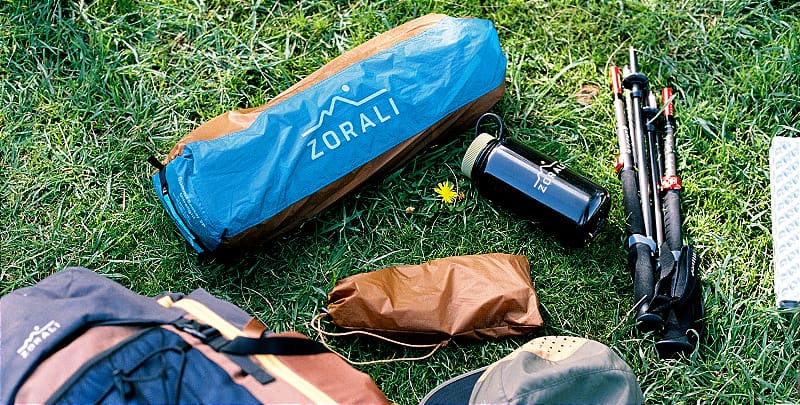 Zorali Summit-Seeker 2P Tent and poles packed down next to backpacking gear and trekking poles Caption: Everything you need, nothing you don’t—this 2P tent packs down small and light for easy hauling into the hills