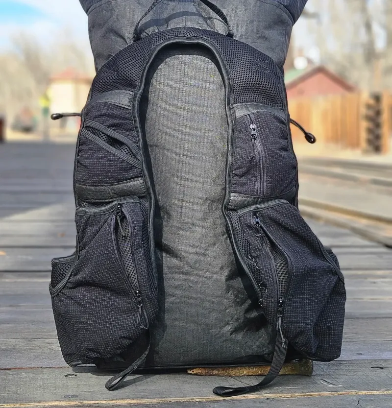 Black Exotic Pack Co Custom FKP ultralight backpack displayed upright on wooden planks with visible pockets and straps.