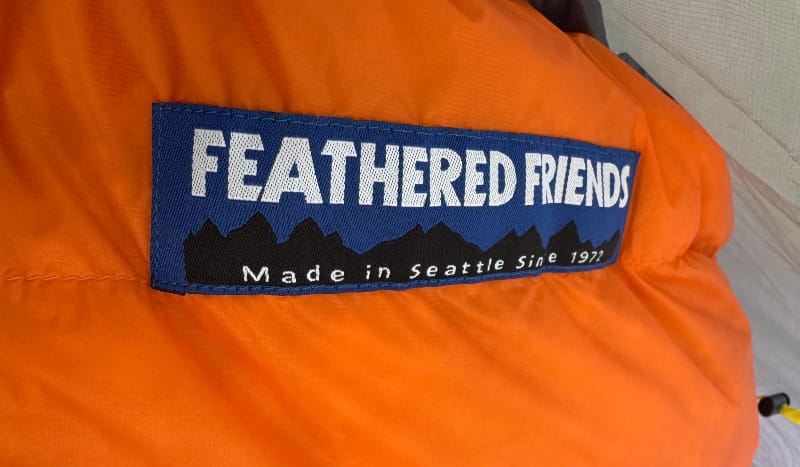 Close-up of Feathered Friends Egret 20° Sleeping Bag logo on orange fabric inside a tent.