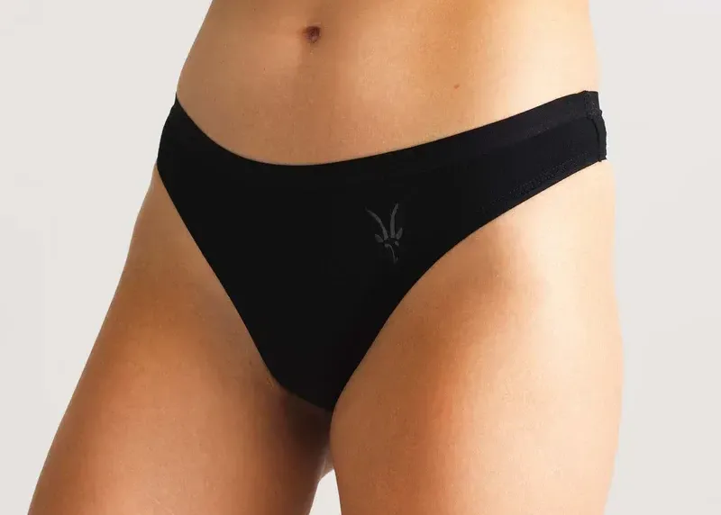Product photo of a woman wearing black Ibex merino wool thong underwear with subtle Ibex logo.