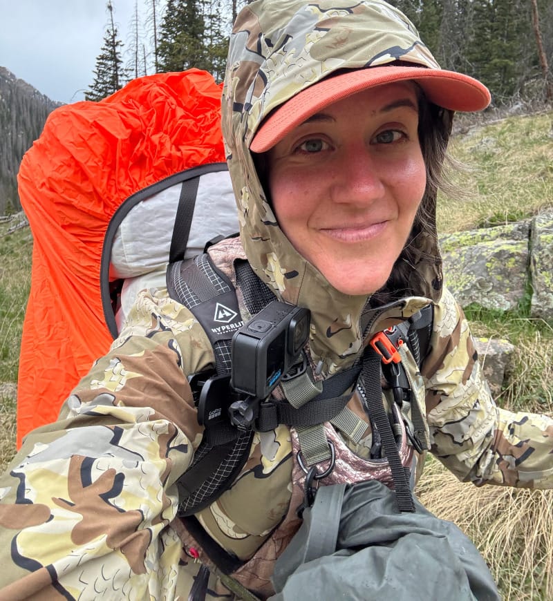 Hiker wearing KUIU Chugach TR Rain Jacket in a mountainous forest during a rainy backpacking trip.