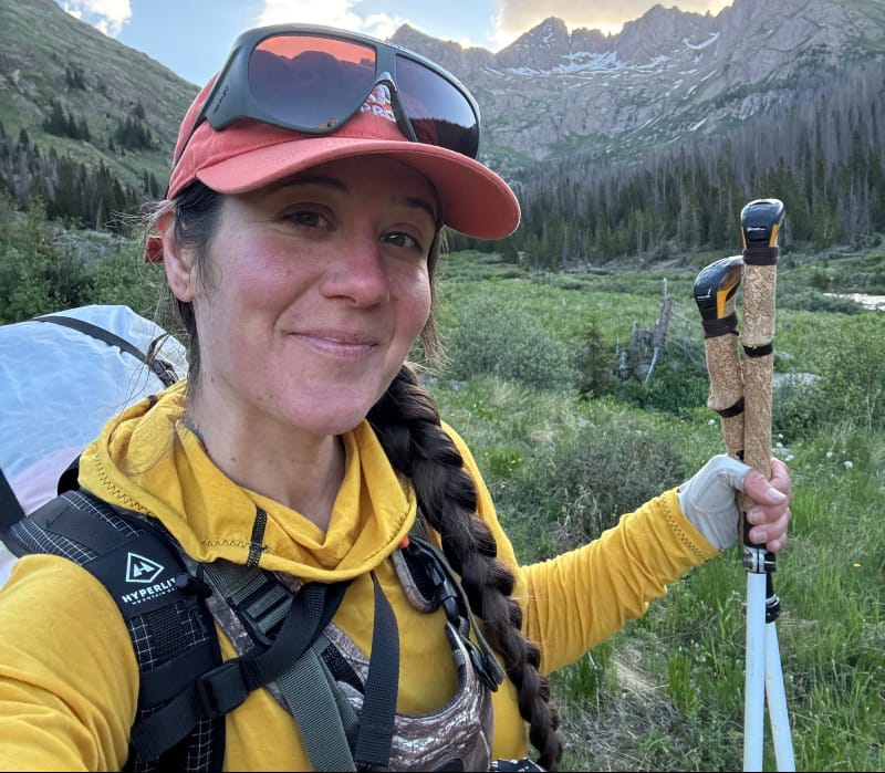  Backpacker wearing Melanzana Merino Base Hoodie and sunglasses, smiling in the mountains during golden hour in the Sangre de Cristos.