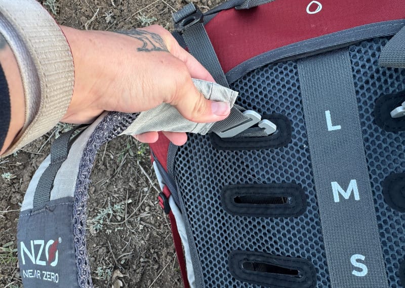  Close-up of a hand adjusting the torso fit on the Dean 60 backpack's shoulder harness system.