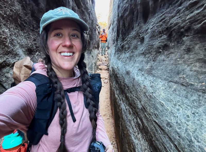  Person hiking through a narrow sandstone canyon wearing the pink PAKA SOL Hoodie and backpack with gear.