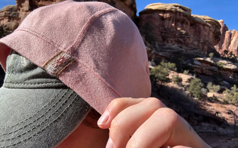 Close-up of PAKA SOL Hoodie hood layered over a ball cap, showcasing stitching detail and sun coverage.