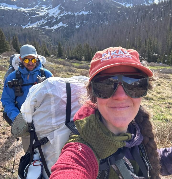Woman hiking in the alpine wearing Vuarnet Altitude 01 sunglasses with snow-covered peaks in the background.