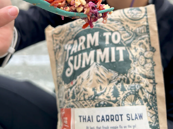 Close-up of a hiker holding a spork of Farm To Summit Thai Carrot Slaw in front of the meal pouch during a backpacking trip.