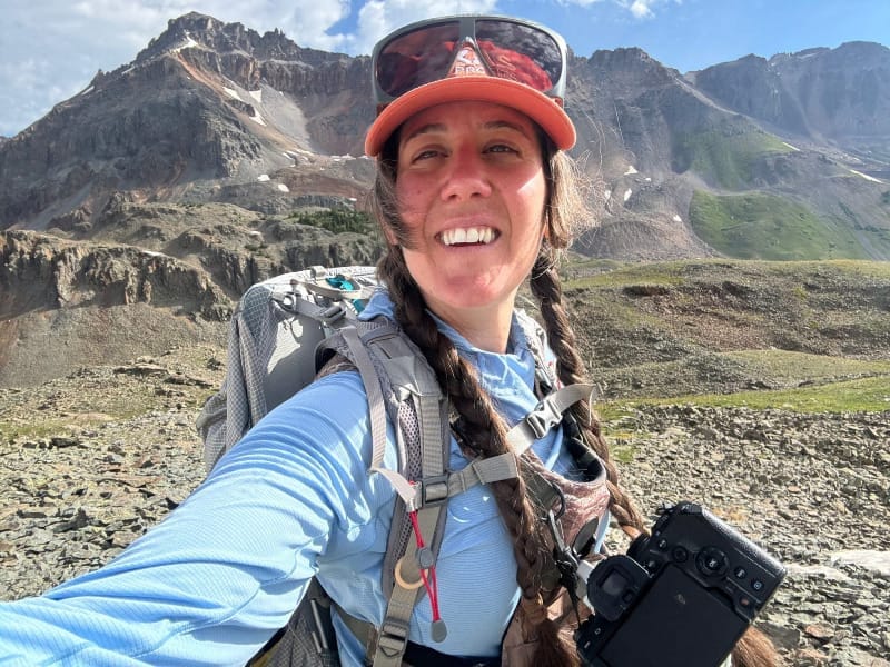 Hiker wearing the Aarn Mountain Magic 50 Pro backpack in the alpine with camera gear and mountain backdrop