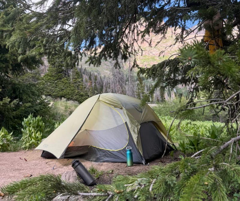 Backpacking tent set up in a forested mountain campsite, ideal for enjoying cold soak meals.