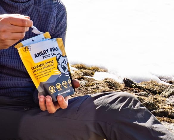 Backpacker eating Angry Pika granola cold soak meal while sitting on alpine tundra with snow patches.