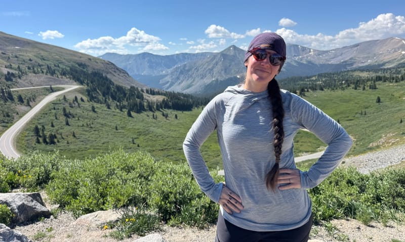 Woman standing in the mountains wearing FKT Gear High Lonesome sunglasses and a sun hoodie.