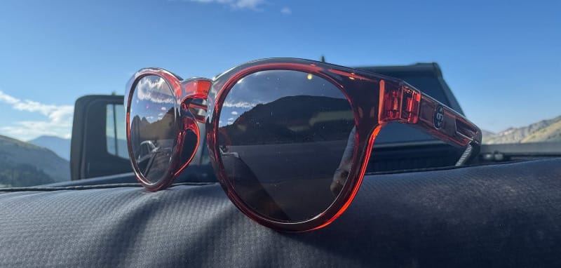 FKT Gear High Lonesome sunglasses on a car dashboard with blue sky and truck in the background.