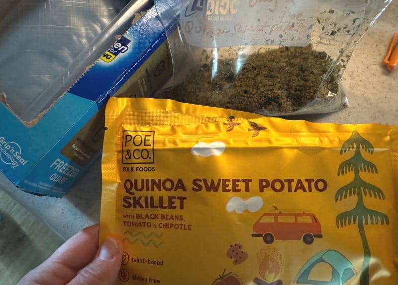  Close-up of Poe & Co Folk Foods Quinoa Sweet Potato Skillet pouch beside a Ziploc meal bag and freezer bag box on a kitchen counter.