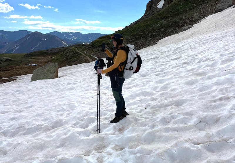  Person wearing a yellow-colored Wuru Wool Lightweight Hoodie hiking across a snowy slope in the San Juan Mountains under a bright sky.