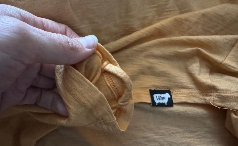  Close-up of a hand holding the cuff of a mustard yellow Wuru Wool hoodie, highlighting fabric texture and brand tag with a sheep logo.