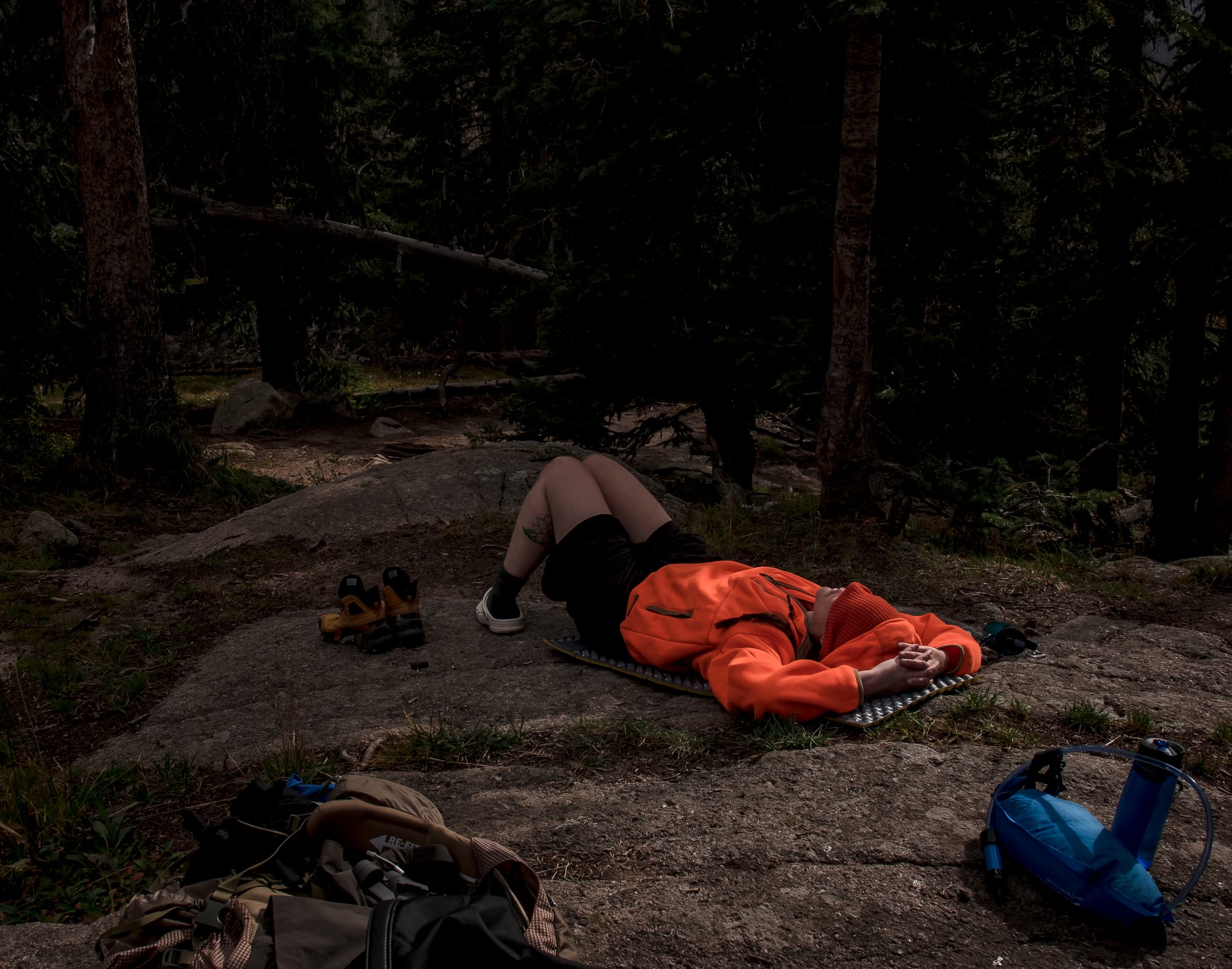 Hiker lying on a foam pad in the forest wearing a blaze orange jacket and hat for visibility during hunting season.