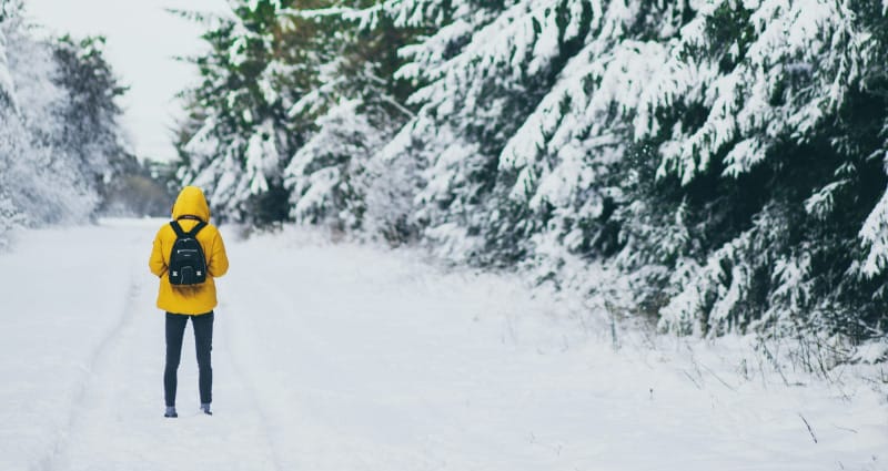 Person in yellow jacket walking snowy forest trail, highlighting outdoor holiday gifts on Amazon 2025.