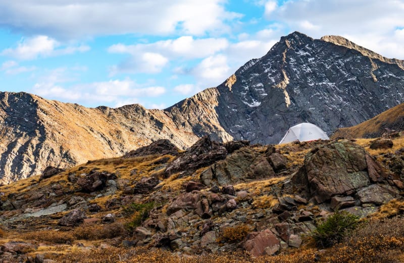 Tent set up in an alpine basin with rocky peaks and early autumn snow patches, showcasing cold-weather camping and backpacking in the mountains.