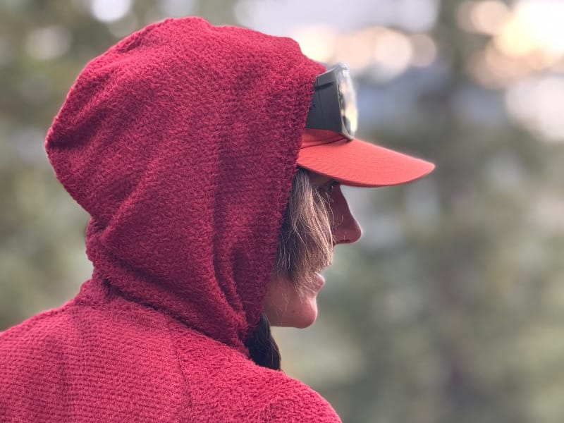 Close-up side profile of a hiker wearing the hood of the FarPointe Alpha Cruiser with a cap underneath in a forested setting.
