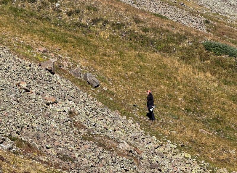 Hiker wearing KUIU Attack Pants while climbing a steep, rocky mountain slope in high alpine terrain.