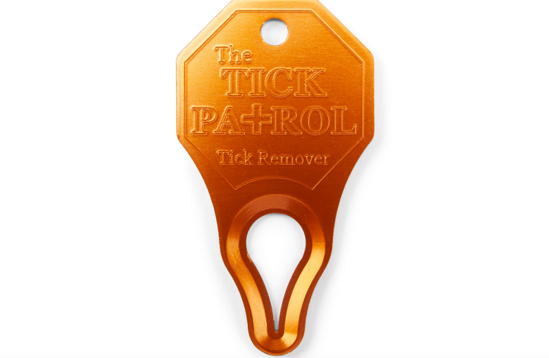 Orange aluminum Tick Patrol tick remover tool designed for outdoor use.